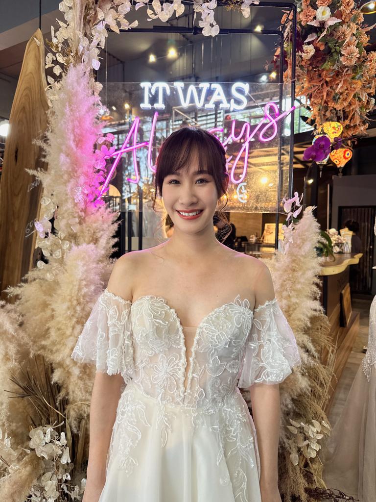A woman in a wedding dress poses gracefully in front of a decorative sign, capturing a moment of celebration.