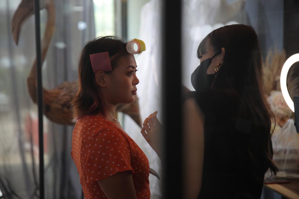 A woman receives makeup application from another woman in a well-lit beauty studio setting.