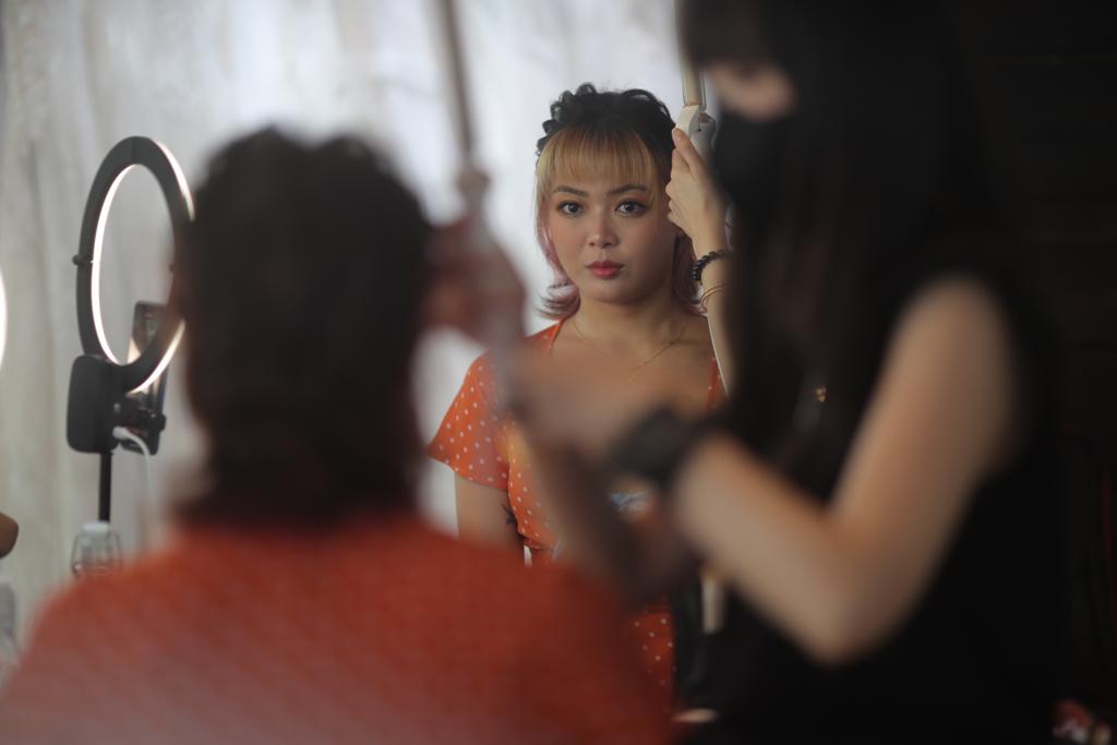 A woman receives makeup application from another woman in a well-lit beauty studio setting.