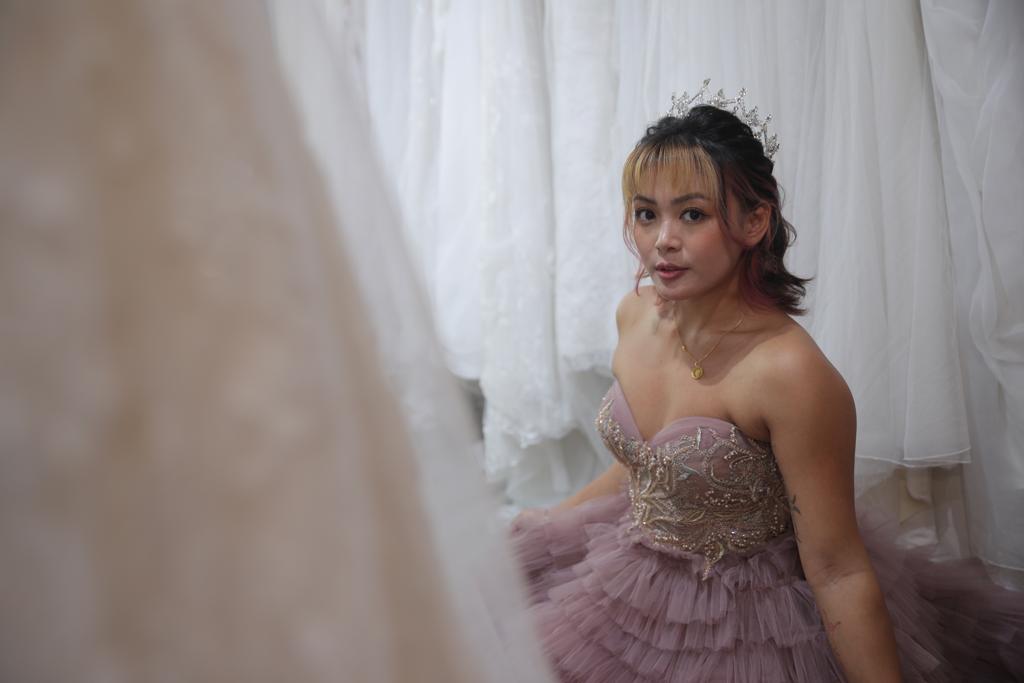 A woman in a wedding dress gazes thoughtfully at various wedding dresses displayed around her.