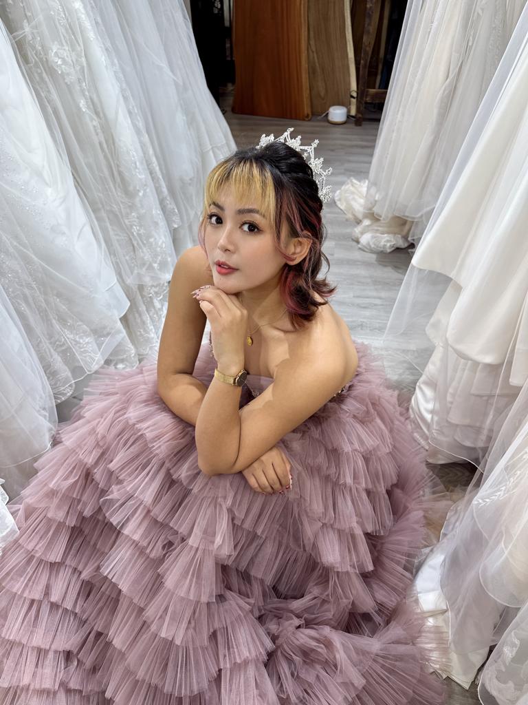 A woman in a wedding dress gazes thoughtfully at various wedding dresses displayed around her.