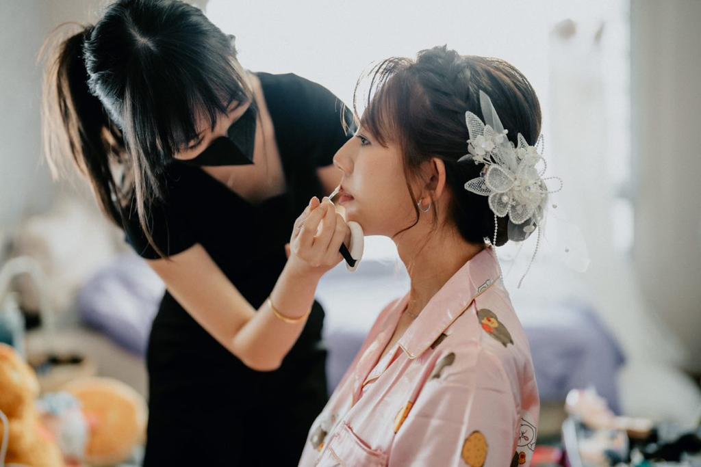 A woman receives makeup application from another woman in a well-lit beauty studio setting.