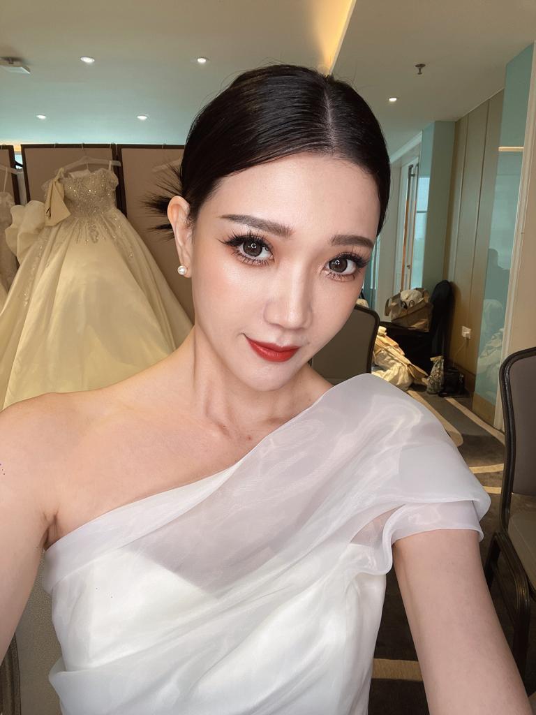 A woman in a white dress smiling while taking a selfie, capturing a moment of joy and elegance.