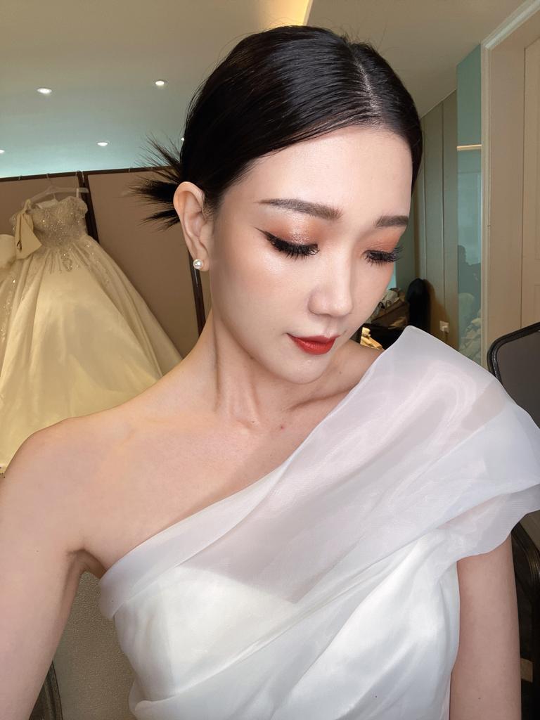 A woman in a white dress smiling while taking a selfie, capturing a moment of joy and elegance.
