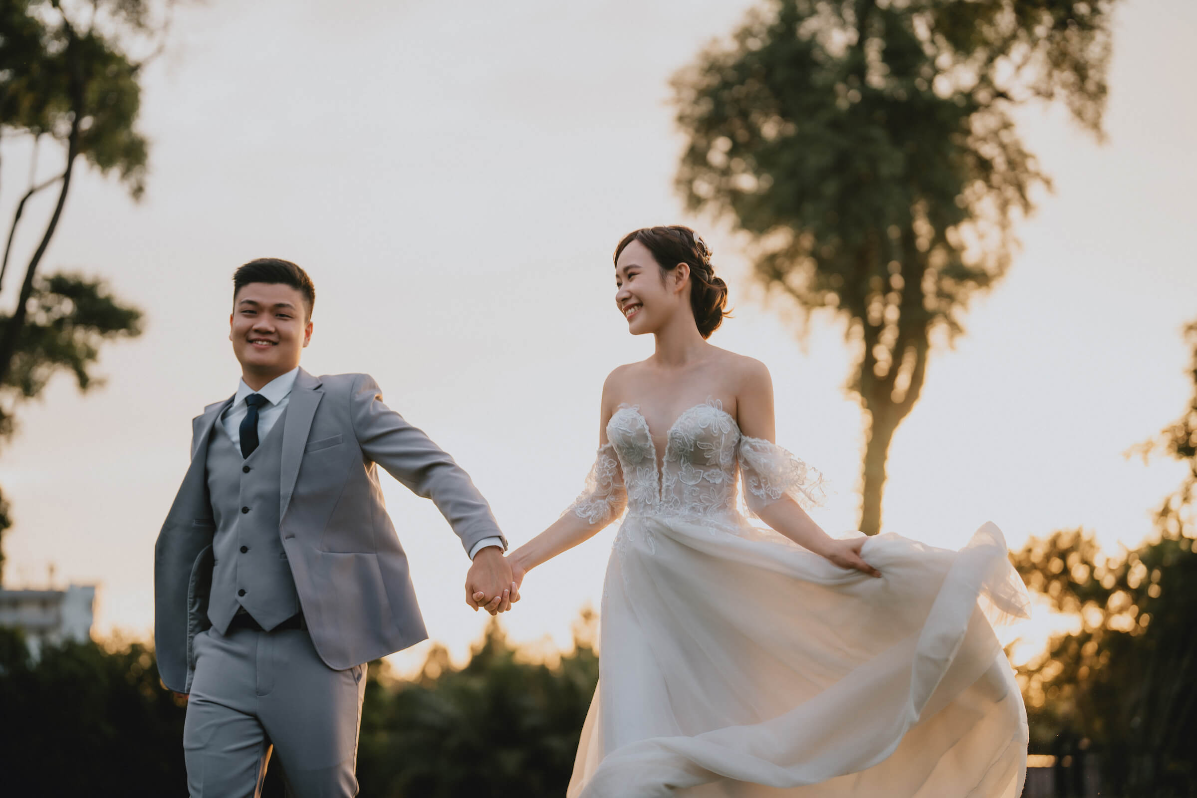 A bride and groom stroll hand in hand across the grass, with a grand mansion in the background.