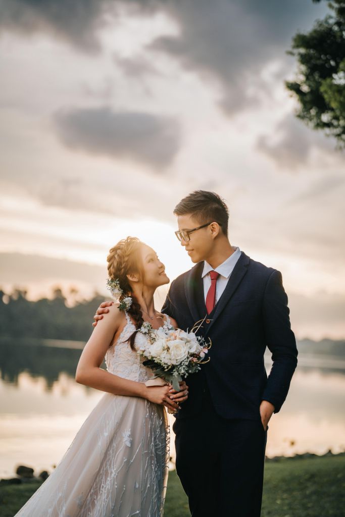 Bride and groom at a lakeside at sunset, bride holding her bouquet