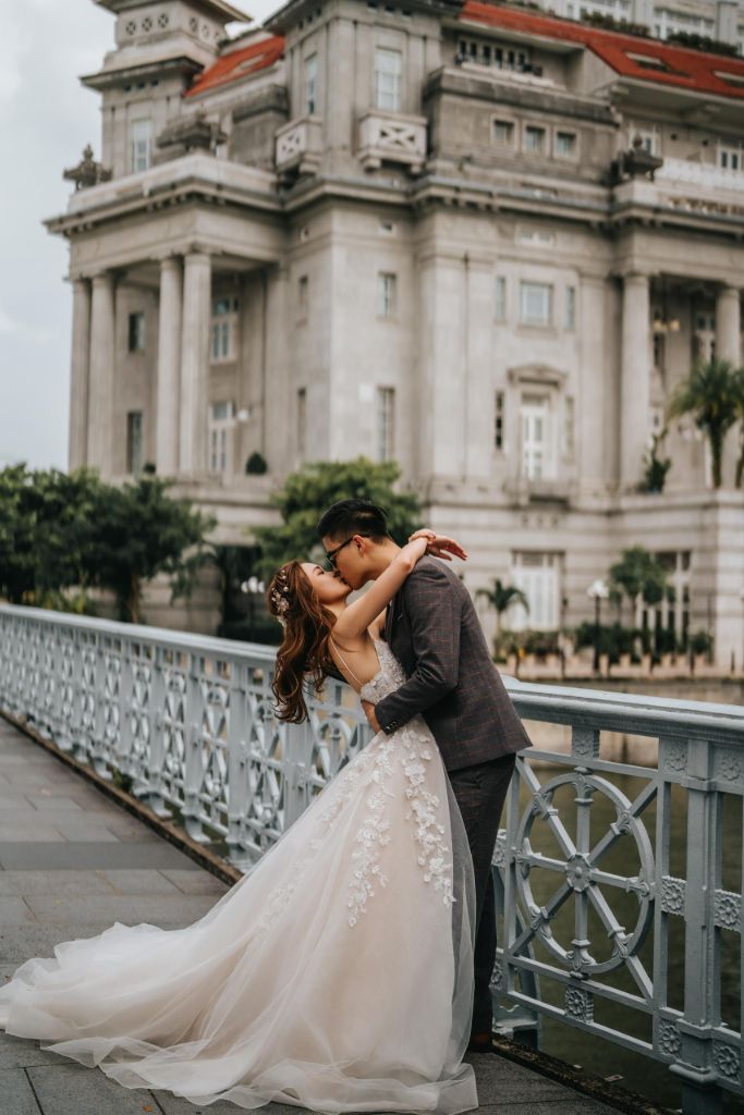 Couple sharing a kiss on a bridge with a heritage mansion behind
